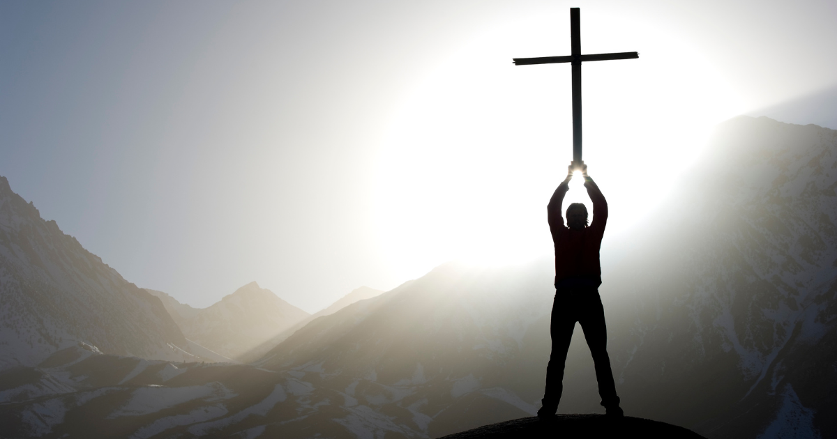 Prayer for strength and healing - man holding a big cross situated in the mountains